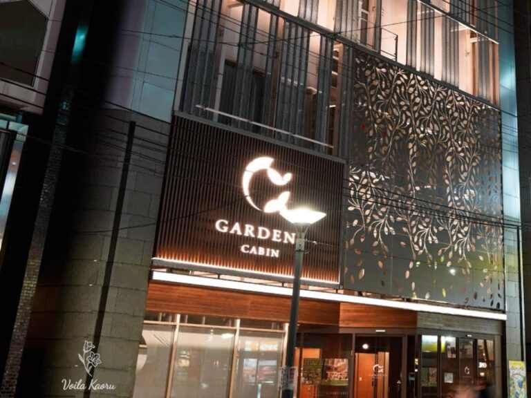 Gardens Cabin entrance at night, with illuminated signage and a decorative leaf-pattern facade