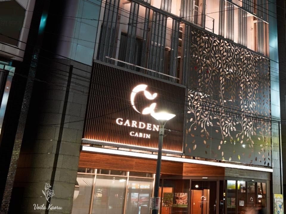 Gardens Cabin entrance at night, with illuminated signage and a decorative leaf-pattern facade