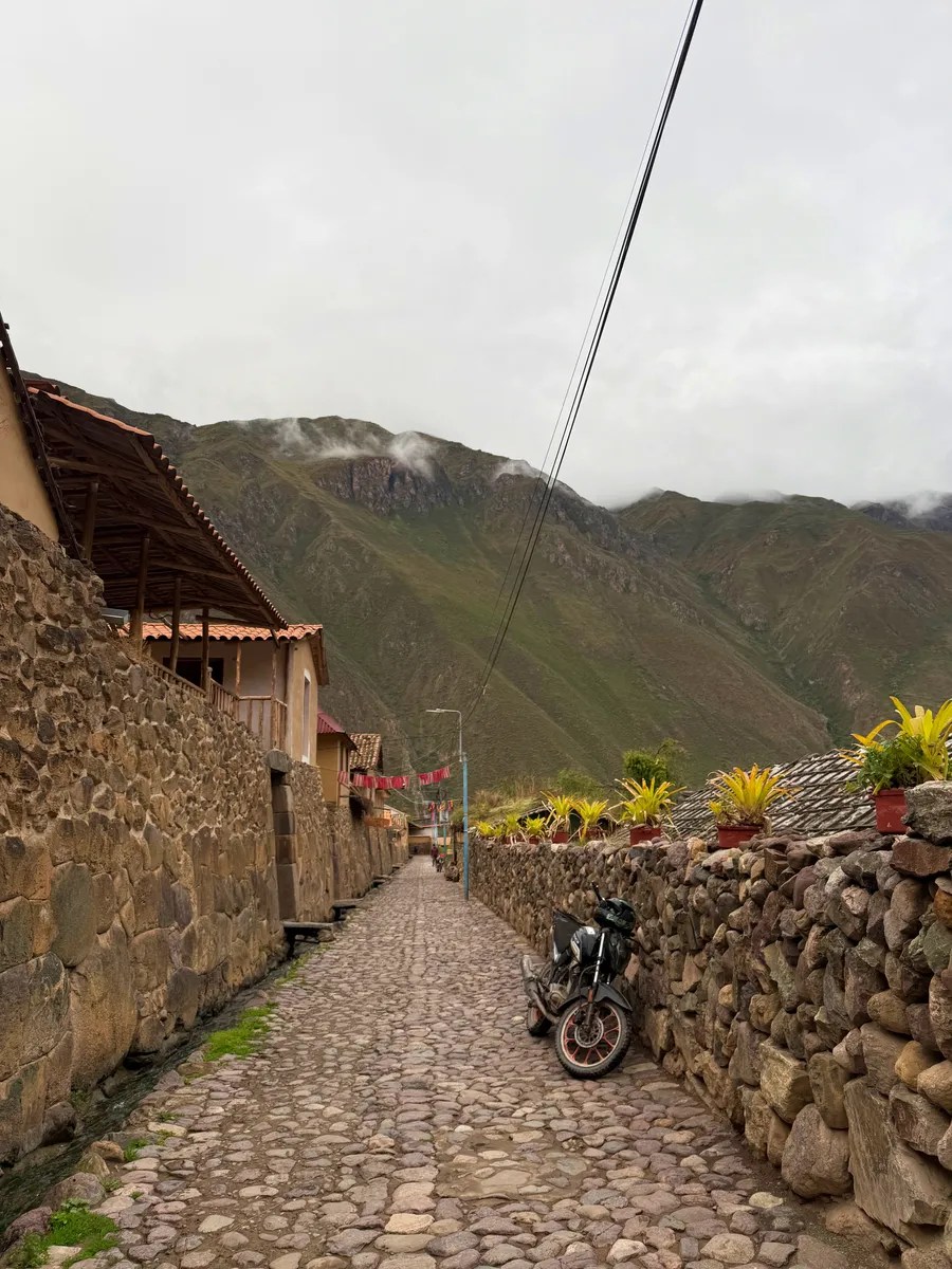 Stone walls and a cobbled lane beneath cloud-covered mountains in Ollantaytambo