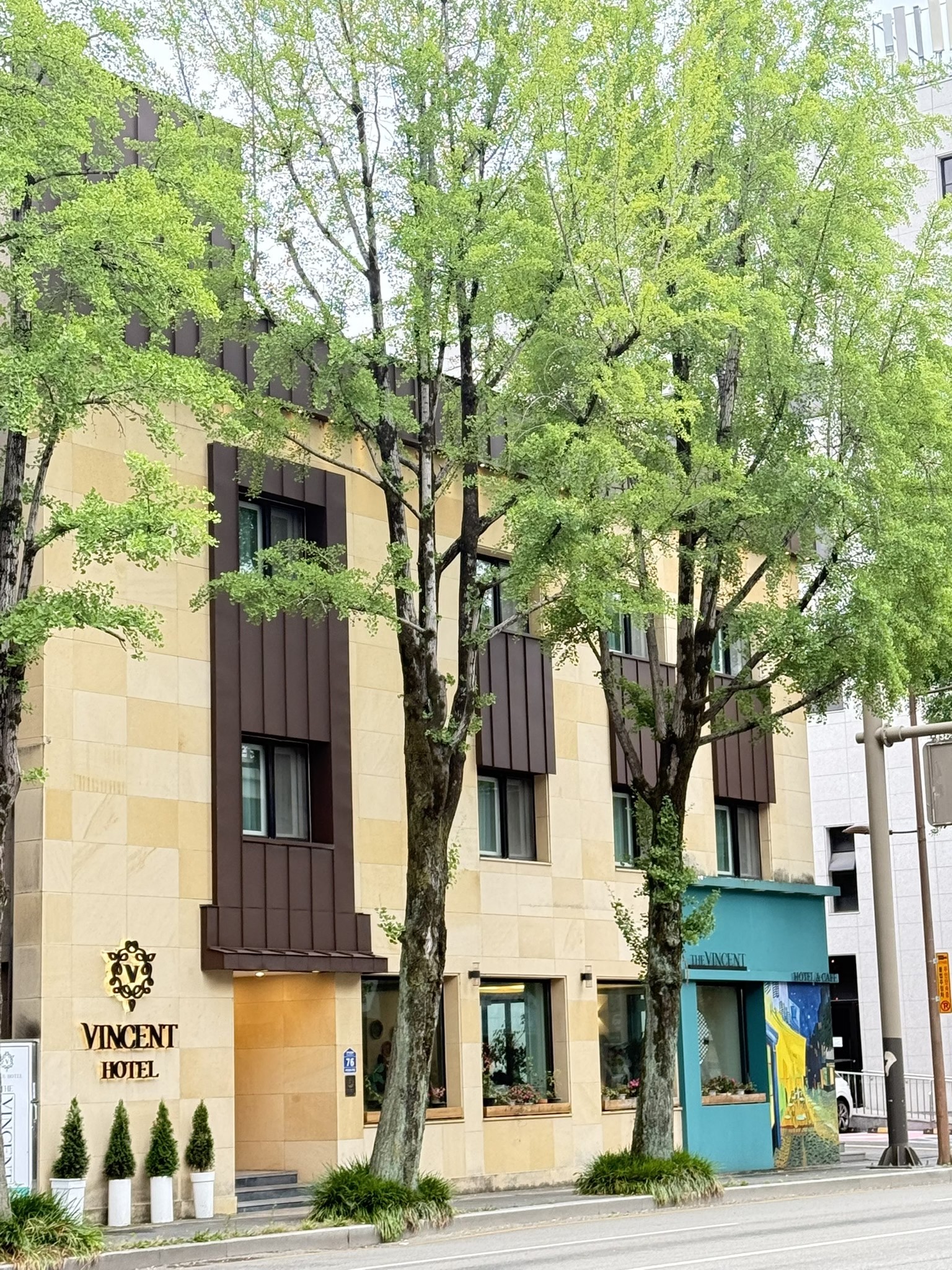 The Vincent Hotel in Jeonju, with a cream facade, turquoise cafe entrance, and leafy street trees