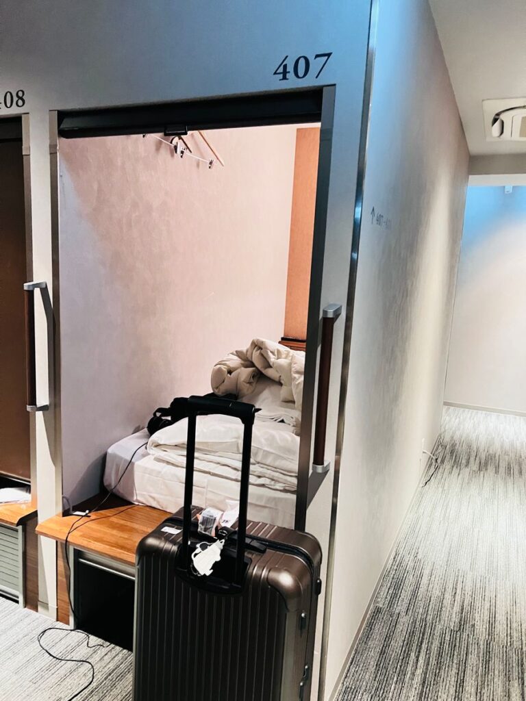 Open cabin at Gardens Cabin Sapporo with a bed and a large suitcase at the entrance