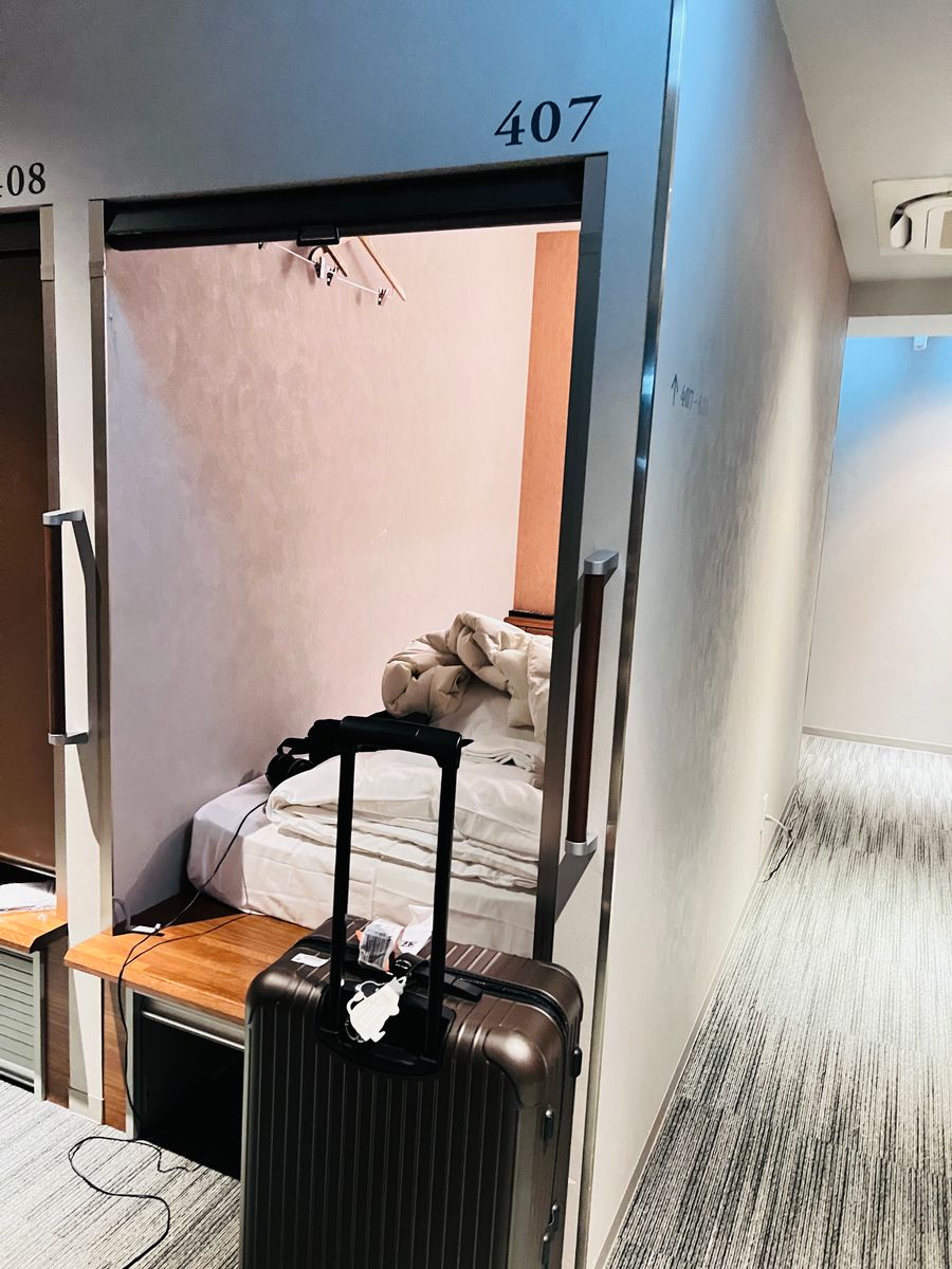 Open cabin at Gardens Cabin Sapporo with a bed and a large suitcase at the entrance