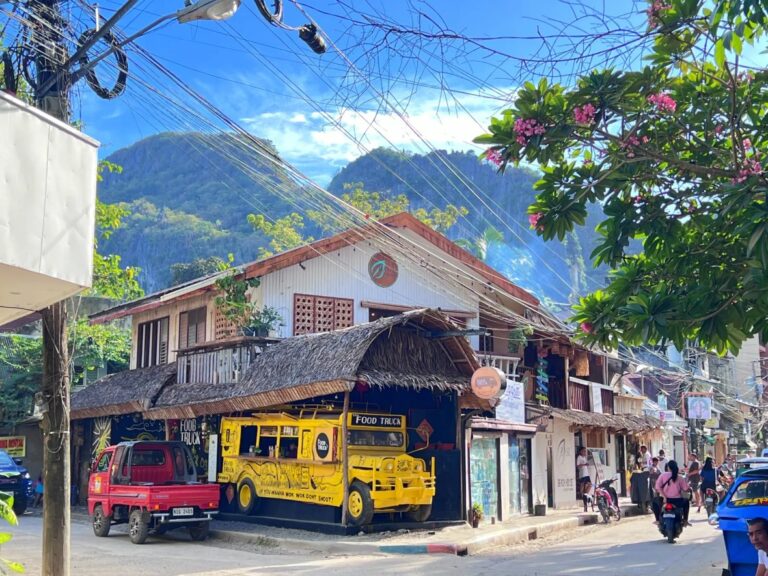 El Nido town street with a yellow food truck, motorcycles and limestone cliffs behind the buildings