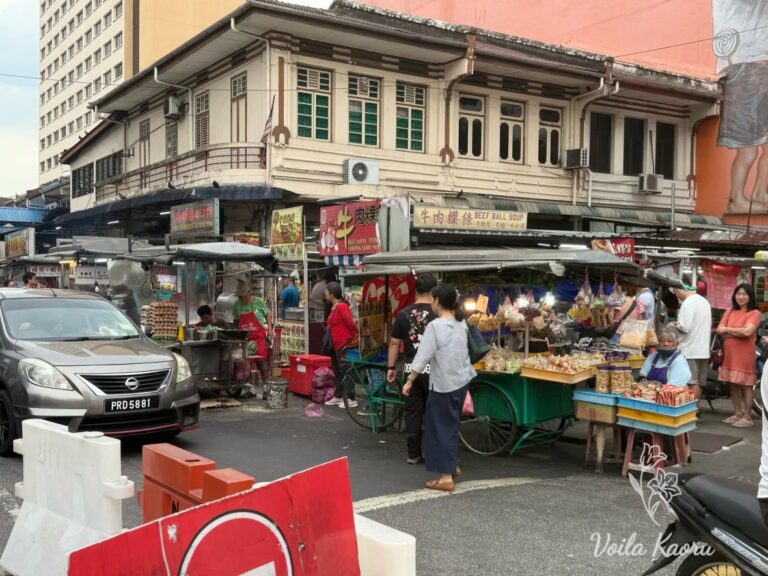 Street food stalls and pedestrians beside cream-colored shophouses in Penang