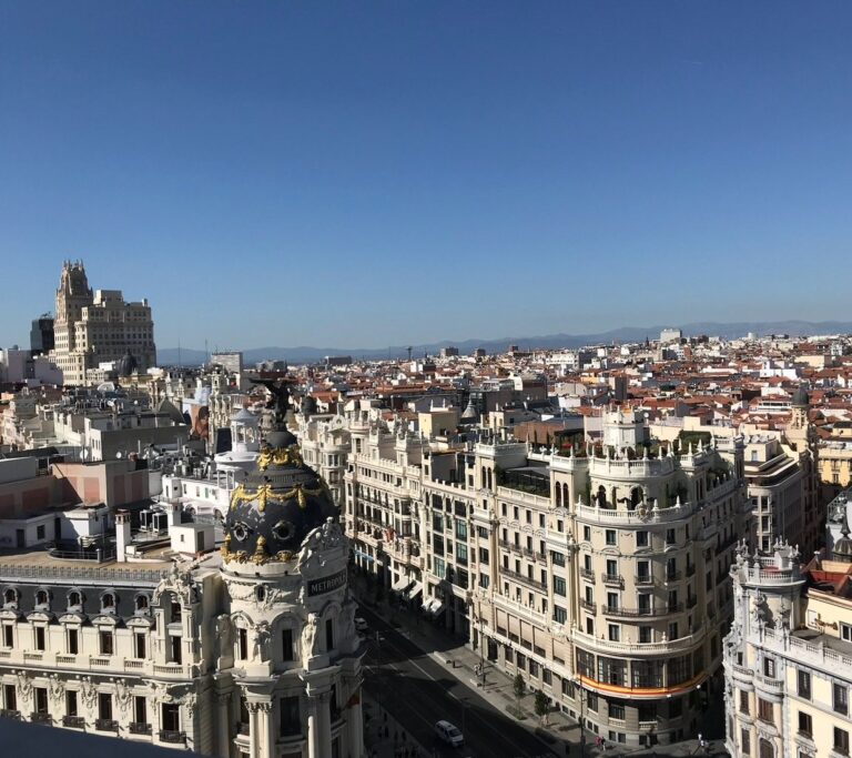 Madrid rooftops and the ornate black-and-gold dome of the Metropolis Building beneath a blue sky